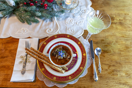 Duck stew and bread sticks on fine China place settings on a Christmas table.