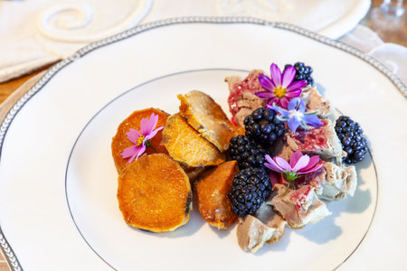 Gourmet plate of duck, blackberries, sauce, and sweet potato on an antique porcelain dish rimmed...
