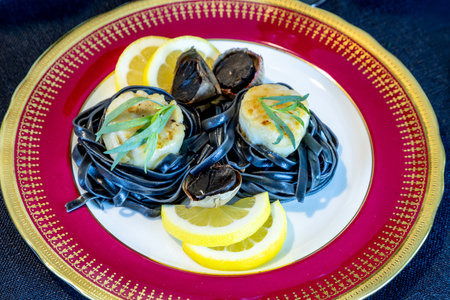 Scallops on a bed of black squid ink pasta with black garlic on a red plate.の写真素材