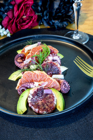 Citrus Octopus salad with blood orange and avocado on a black plate.の写真素材