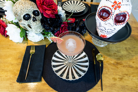 Table with a red velvet skull shaped cake and a grapefruit margarita on a black plate on an All Saints Day decorated table.の写真素材