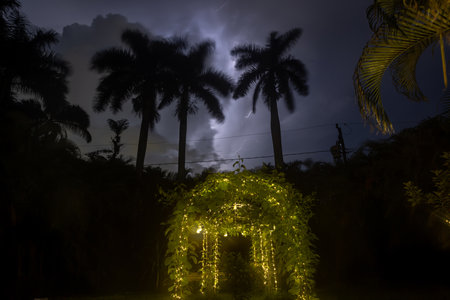 Lightning illuminates the night sky over a backyard with fairy lights along a vine arch.