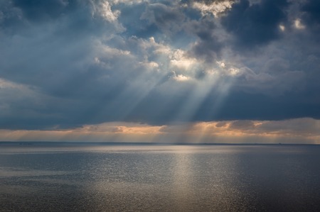 Sun beam through heavy sky over calm Mediterranean sea. Sicily coast, Italyの写真素材