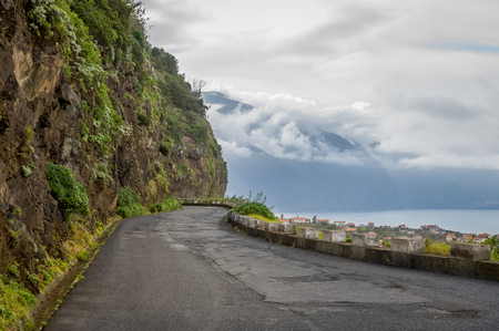 Old mountain road between steep mountain wall and cliff to the ocean. North coast of Madeira island, Portugal.の写真素材