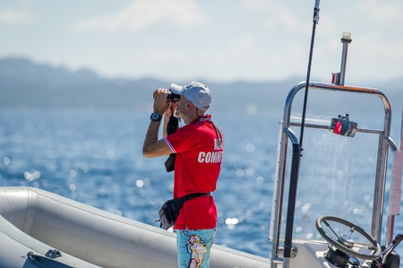 Sailing race referee is watching at his binocular, standing on the race commitee RIB boat. Sardinia,...