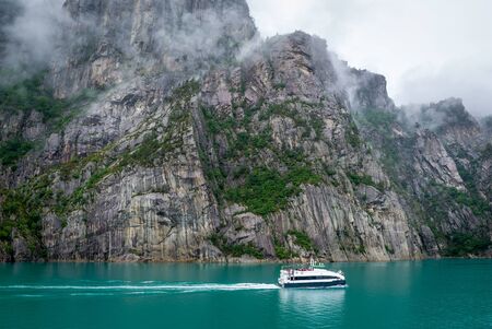 Small touristic ferry at beautiful fjord with rocky shores and tourquise water. Lysefjord, Norway.の写真素材