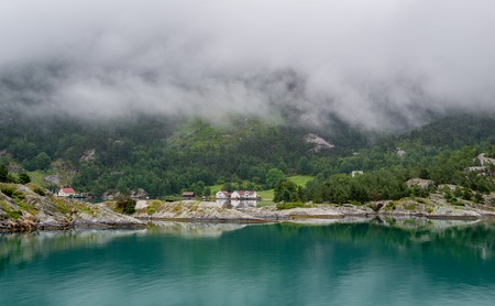 Houses of norwegian village at fjord's shores . Clouds are hiding mountain peaks above the town. Lysefjord, Norway.の写真素材