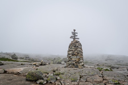 Big stone pyramid with hiking path route sign on the hiking path to Kjeragbolten. Landscape in the strong mountain fog. Lysefjord, Norway.の写真素材