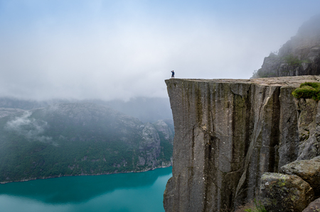 Tourist is standing at the cliff of famous norwegian touristic attraction - Prekestolen rock. Lysefjord, Rogaland, Norway.の写真素材