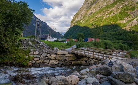 Small wooden bridge at mountain river and evening fjord landscape. Neroy fjord garden, Norway.の写真素材