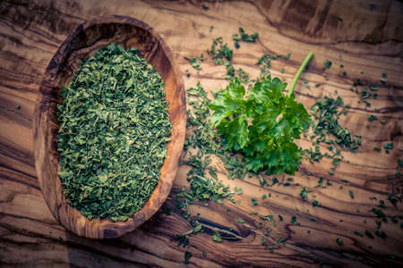 dried rubbed and fresh parsley on olive woodの写真素材
