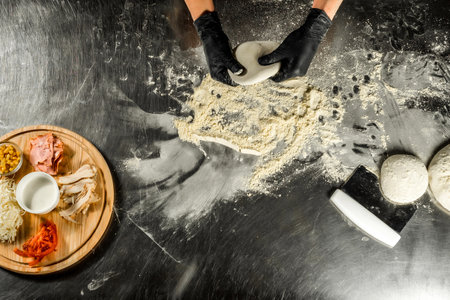 Female hands in black gloves kneading dough on a metal tableの写真素材