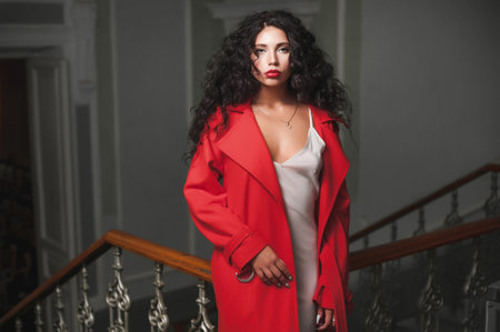 Fashionable young woman with curly hair in red coat in the interior