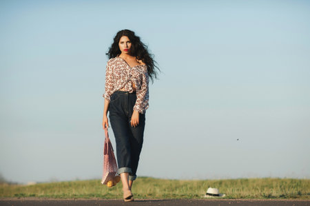 Outdoor portrait of beautiful young woman walking on the road in summer.