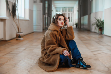 Portrait of a beautiful young woman in a beige coat sitting on the floor.