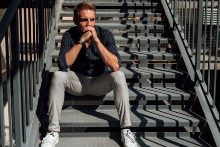 Handsome young man in casual clothes sitting on stairs and looking awayの写真素材