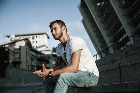 Portrait of a handsome young man in casual clothes sitting on the stairs outdoors.の写真素材