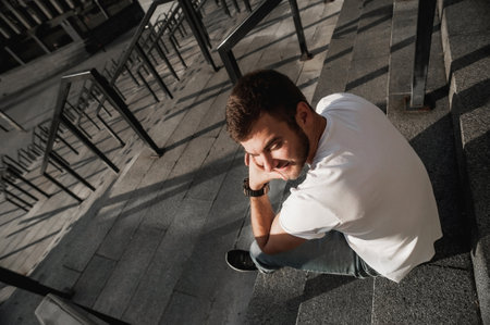 Top view of a pensive young man sitting on the stairs outdoors