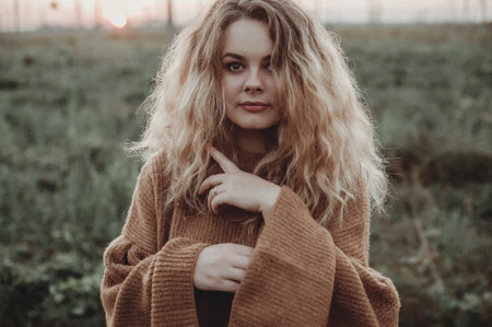 Portrait of a beautiful blonde girl with long curly hair in a brown sweater in the field.