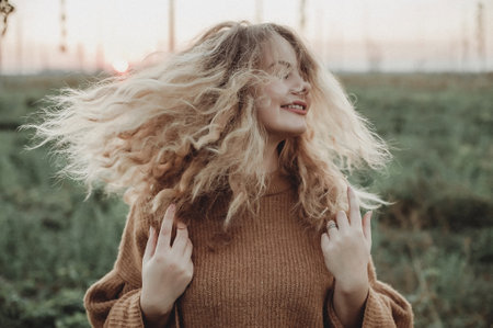 Beautiful blonde girl with long curly hair in the field at sunsetの写真素材
