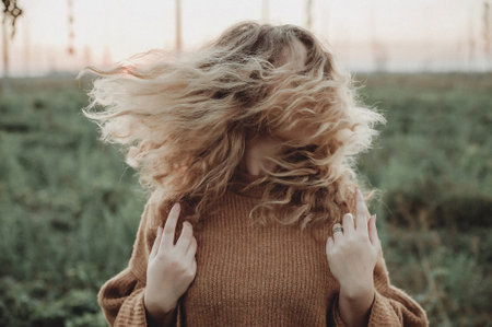 Beautiful girl with blond curly hair in the field at sunset.の写真素材