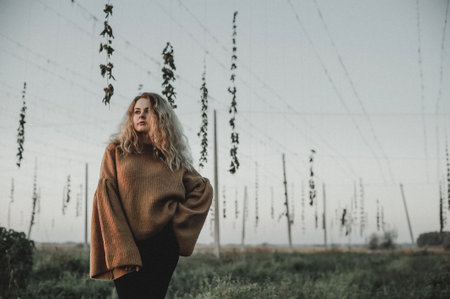 Beautiful girl with long blond hair posing in a field with high voltage wires.の写真素材