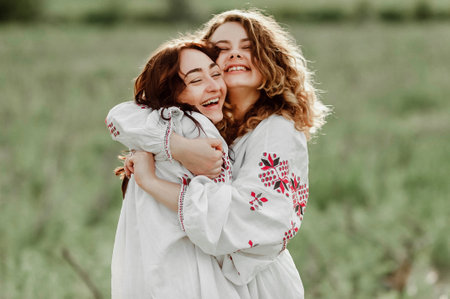 Two young women in embroidery are hugging each other in the fieldの写真素材