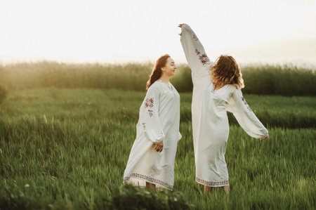 Two beautiful women in white clothes walking in the field at sunset.の写真素材