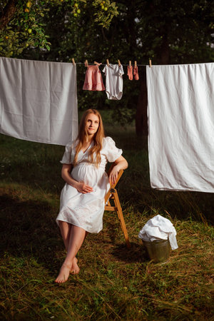 Beautiful pregnant woman drying clothes on a clothesline in the gardenの写真素材