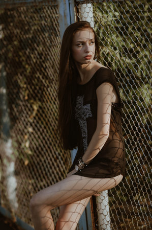 Young beautiful girl in a black dress on the background of the fence