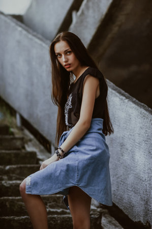 Portrait of a beautiful brunette girl in a denim skirt on the stairs.