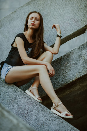 young beautiful long-haired brunette woman in jeans shorts posing on stairsの写真素材