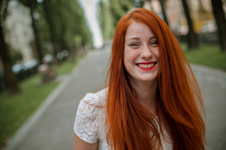 Redhead girl with freckles in a white dress on the streetの写真素材