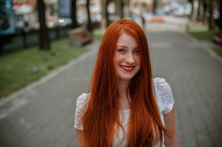 Redhead girl with long hair in white dress on the street.の写真素材
