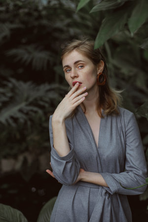 A girl poses in a botanical garden among plants. The model is wearing a gray suit. Freckles on the girl's face. The girl poses among flowers, bushes, trees, cacti.の写真素材