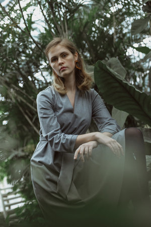 A girl poses in a botanical garden among plants. The model is wearing a gray suit. Freckles on the girl's face. The girl poses among flowers, bushes, trees, cacti.の写真素材