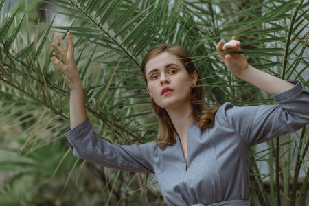 A girl poses in a botanical garden among plants. The model is wearing a gray suit. Freckles on the girl's face. The girl poses among flowers, bushes, trees, cacti.の写真素材