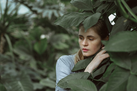 A girl poses in a botanical garden among plants. The model is wearing a gray suit. Freckles on the girl's face. The girl poses among flowers, bushes, trees, cacti.の写真素材
