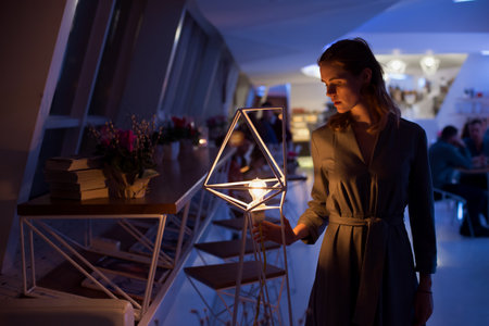 The girl poses in a cafe. The model is wearing a gray suit. Freckles on the girl's face. A fair-haired girl poses in a lit room near a lampの写真素材