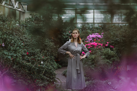 A girl poses in a botanical garden among plants. The model is wearing a gray suit. Freckles on the girl's face. The girl poses among flowers, bushes, trees, cacti.の写真素材