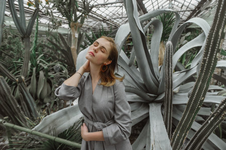 A girl poses in a botanical garden among plants. The model is wearing a gray suit. Freckles on the girl's face. The girl poses among flowers, bushes, trees, cacti.の写真素材