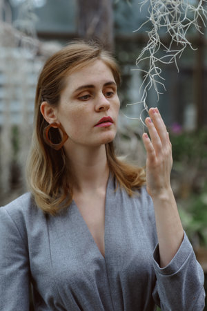 A girl poses in a botanical garden among plants. The model is wearing a gray suit. Freckles on the girl's face. The girl poses among flowers, bushes, trees, cacti.の写真素材