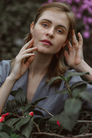 A girl poses in a botanical garden among plants. The model is wearing a gray suit. Freckles on the girl's face. The girl poses among flowers, bushes, trees, cacti.の写真素材