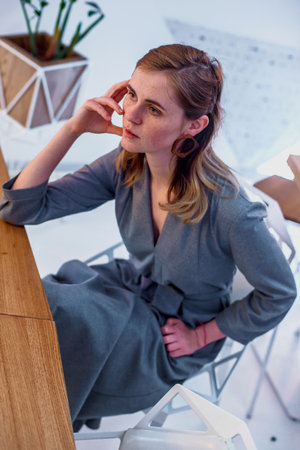 The girl poses in a cafe. The model is wearing a gray suit. Freckles on the girl's face. A fair-haired girl poses in a lit room near a lampの写真素材