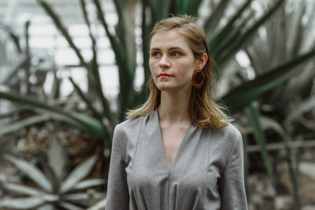 A girl poses in a botanical garden among plants. The model is wearing a gray suit. Freckles on the girl's face. The girl poses among flowers, bushes, trees, cacti.の写真素材