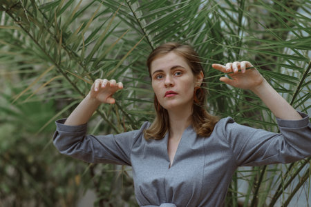 A girl poses in a botanical garden among plants. The model is wearing a gray suit. Freckles on the girl's face. The girl poses among flowers, bushes, trees, cacti.の写真素材