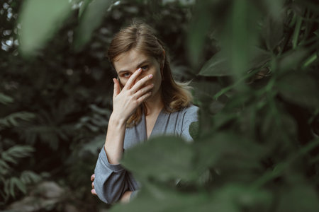 A girl poses in a botanical garden among plants. The model is wearing a gray suit. Freckles on the girl's face. The girl poses among flowers, bushes, trees, cacti.の写真素材