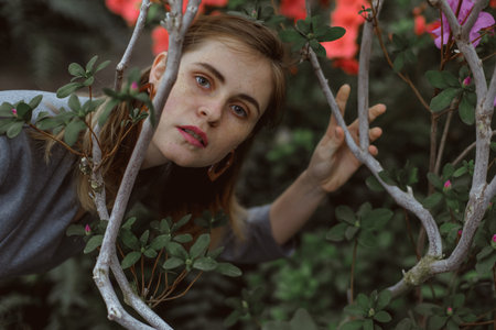 A girl poses in a botanical garden among plants. The model is wearing a gray suit. Freckles on the girl's face. The girl poses among flowers, bushes, trees, cacti.の写真素材