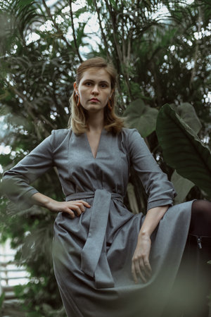 A girl poses in a botanical garden among plants. The model is wearing a gray suit. Freckles on the girl's face. The girl poses among flowers, bushes, trees, cacti.の写真素材