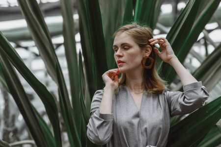 A girl poses in a botanical garden among plants. The model is wearing a gray suit. Freckles on the girl's face. The girl poses among flowers, bushes, trees, cacti.の写真素材